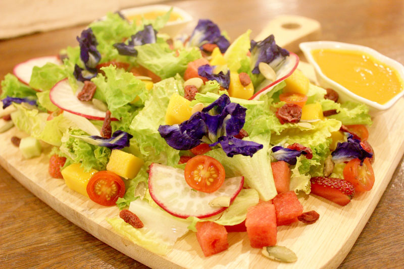 Flower Salad with edible purple flowers, fresh greens, mango, watermelon, and carrot dressing